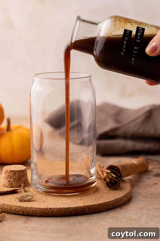 Hand pouring pumpkin spice syrup into a coffee cup with milk