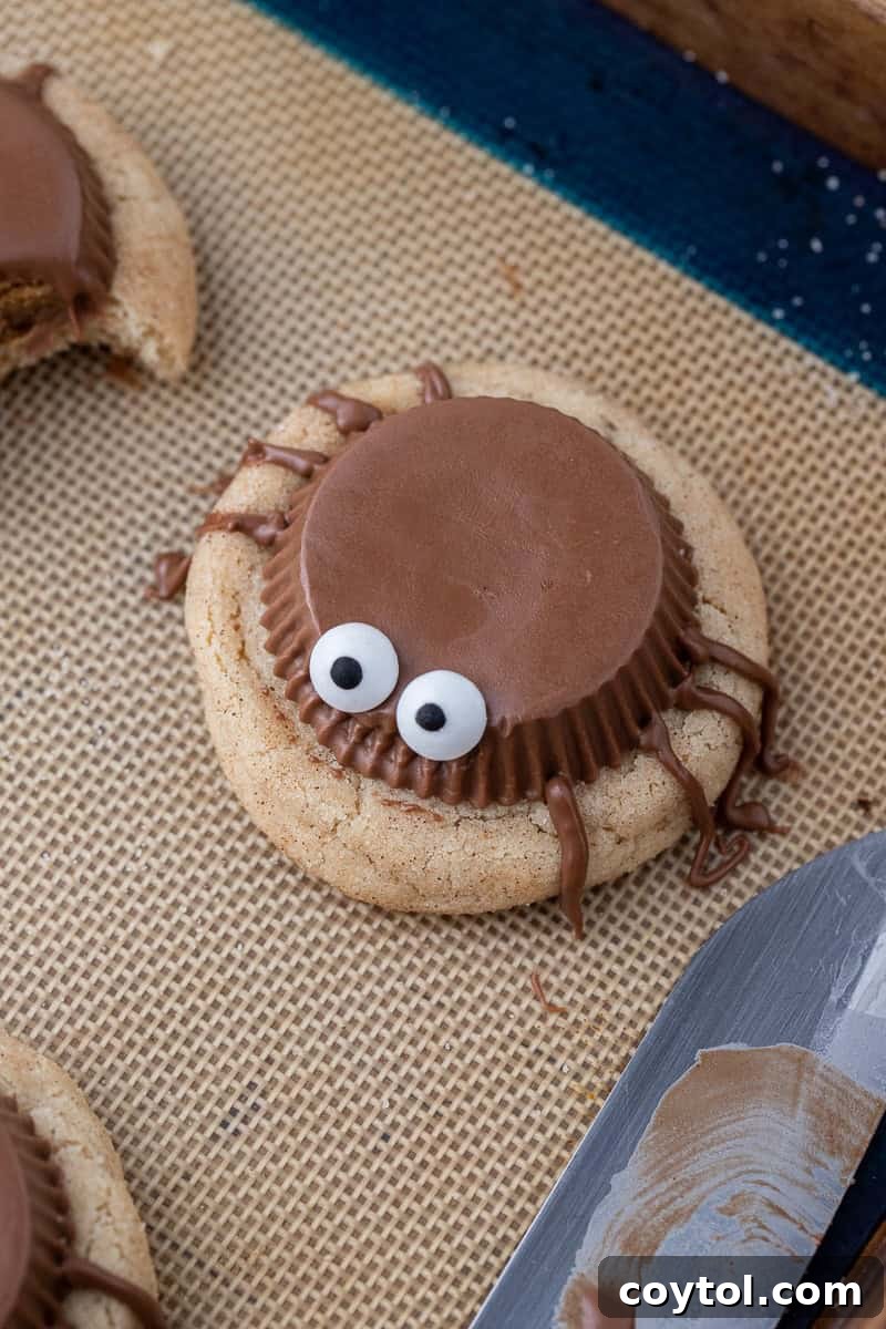 Spooky spider cookies on baking sheet, fully decorated with Reese's, candy eyeballs, and chocolate legs.