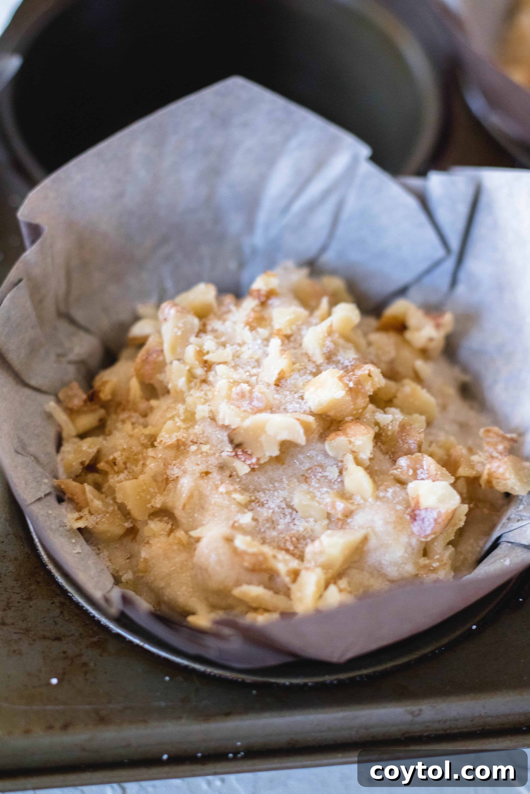 Topping muffins with sugar and walnuts before baking.