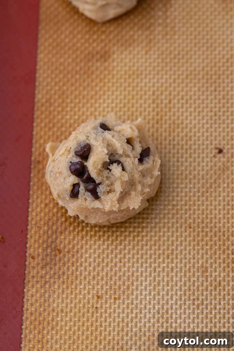 Scooped eggless chocolate chip cookie dough balls placed on a parchment-lined baking sheet, ready for the oven.