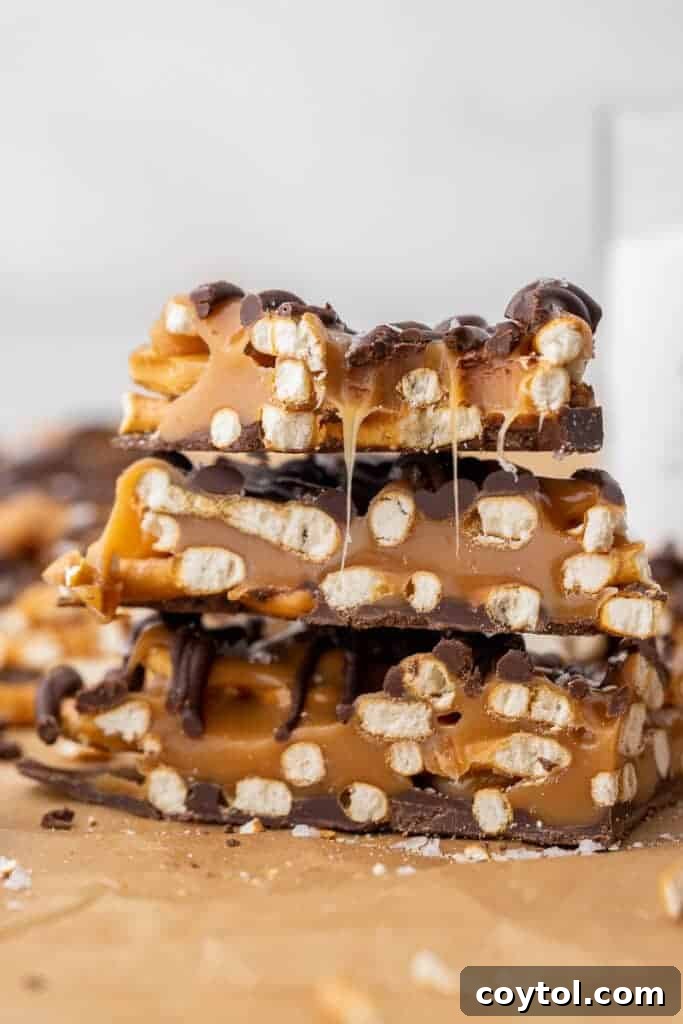 A stack of ooey gooey salted caramel pretzel bark pieces on parchment paper. 