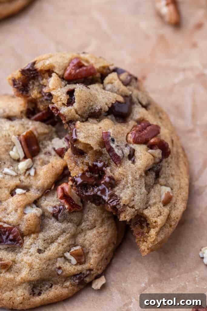 A perfectly baked brown butter pecan chocolate chip cookie, expertly broken in half to showcase its irresistible soft, chewy center filled with melted chocolate and crunchy pecan pieces.