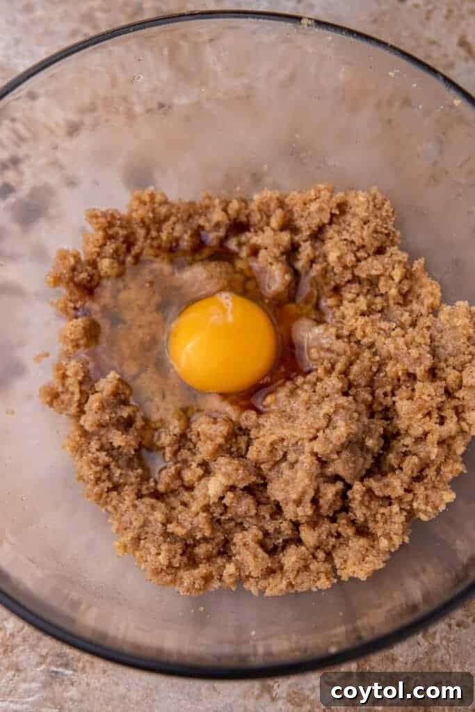 A close-up of wet ingredients, including browned butter, sugars, egg, and vanilla, perfectly mixed in a large bowl, ready for dry ingredients.