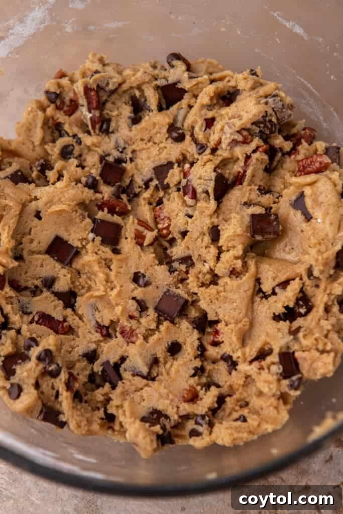 A close-up shot revealing the rich, textured cookie dough in a mixing bowl, showcasing the incorporated chocolate chips and pecan pieces.