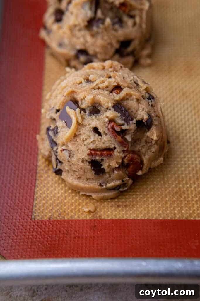 A perfectly portioned ball of brown butter pecan chocolate chip cookie dough resting on a parchment-lined baking tray, ready for the oven.