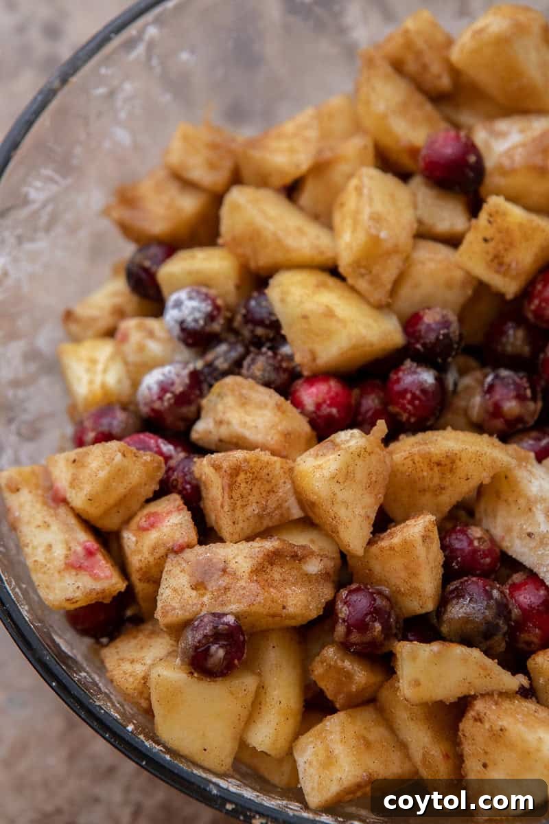 A bowl of fresh apples and cranberries mixed with brown sugar, corn starch, cinnamon, and nutmeg for the fruit filling.