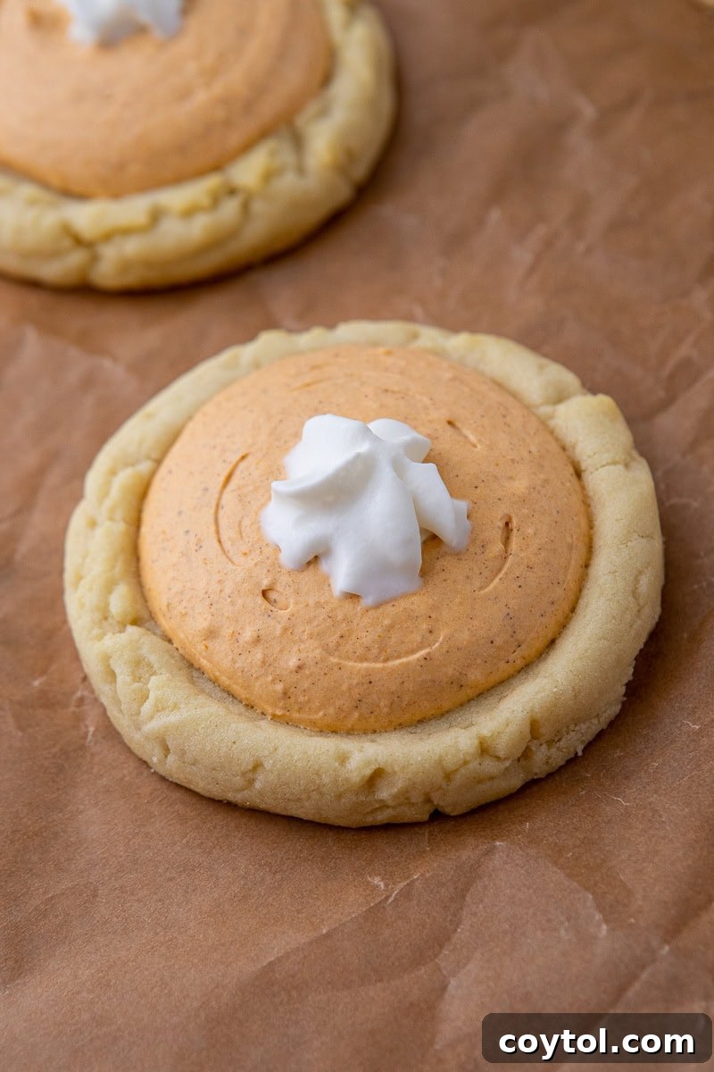 Crumbl's Divine Pumpkin Pie Cookies 10 A tray of freshly baked Crumbl pumpkin pie cookies, each topped with a generous dollop of creamy pumpkin filling and a swirl of whipped cream.