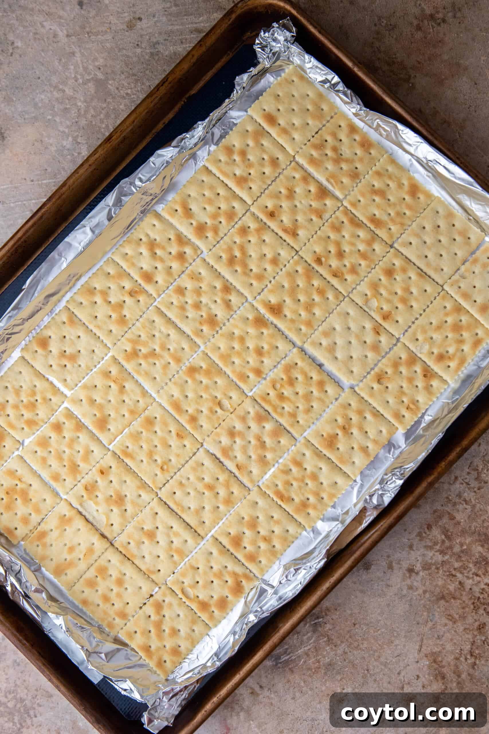 Saltine crackers laid out in a single layer on a foil-lined baking sheet.