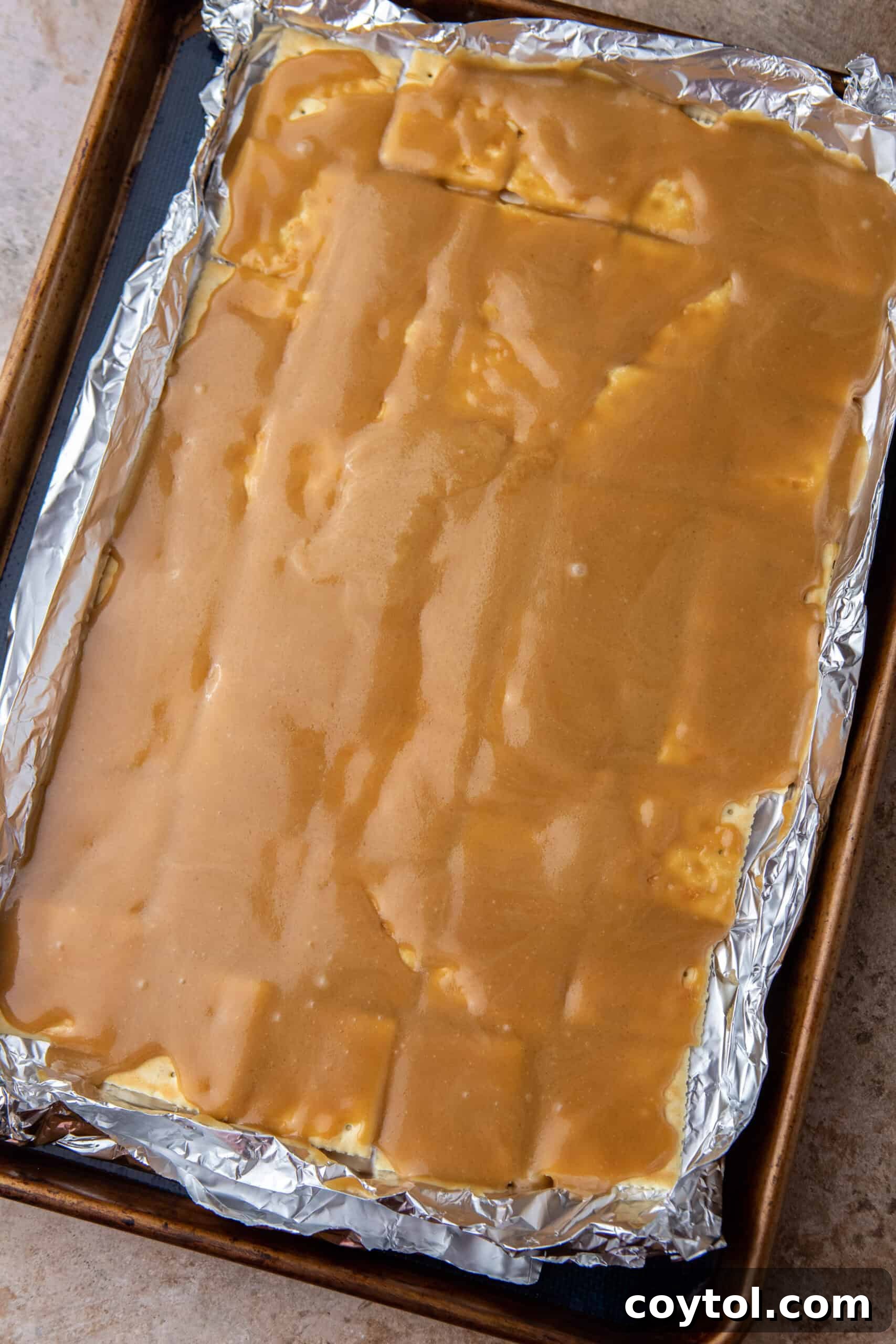 Golden toffee mixture freshly poured over saltine crackers on a baking sheet.