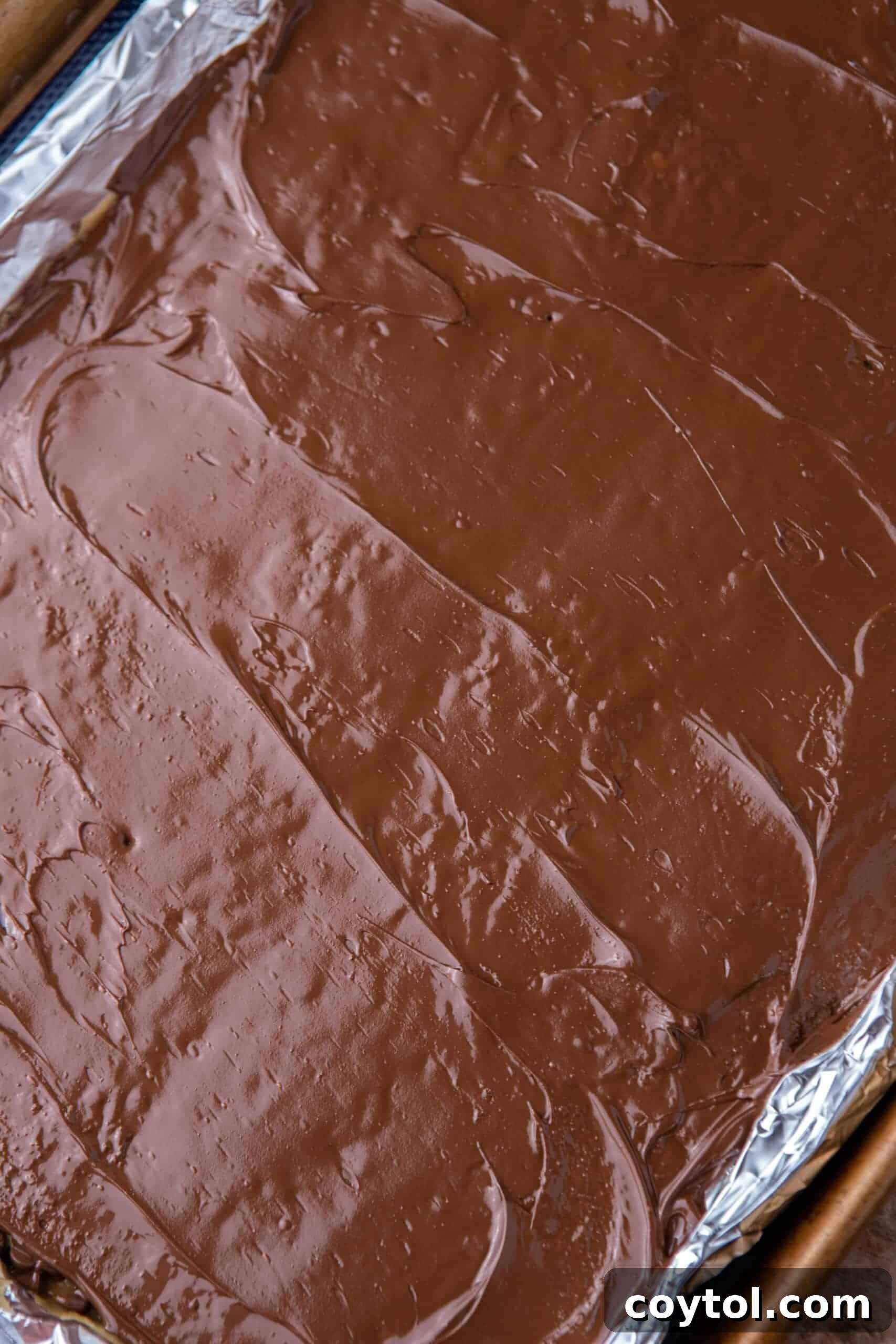 Melted chocolate spread smoothly over the toffee and crackers, forming an even layer.