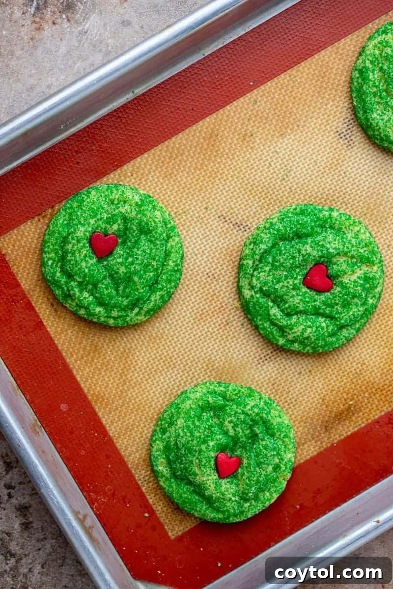 Freshly baked Grinch sugar cookies cooling on a wire rack, their vibrant green and red hearts standing out.
