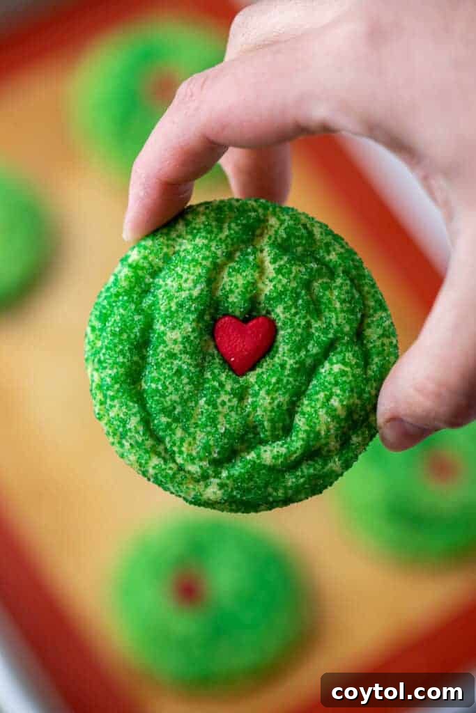 A cluster of vibrant Grinch sugar cookies, fresh from the oven, showcasing their perfect round shape and the iconic red heart sprinkle on each.