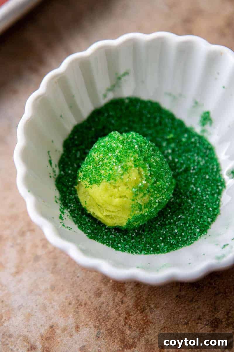 Cookie dough balls rolled in green sugar sprinkles, ready for baking to enhance the Grinch theme.