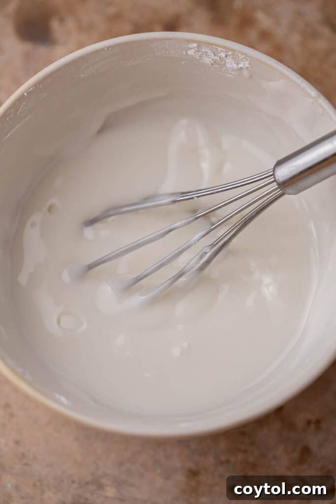 A whisk mixing smooth white sugar cookie icing in a bowl.