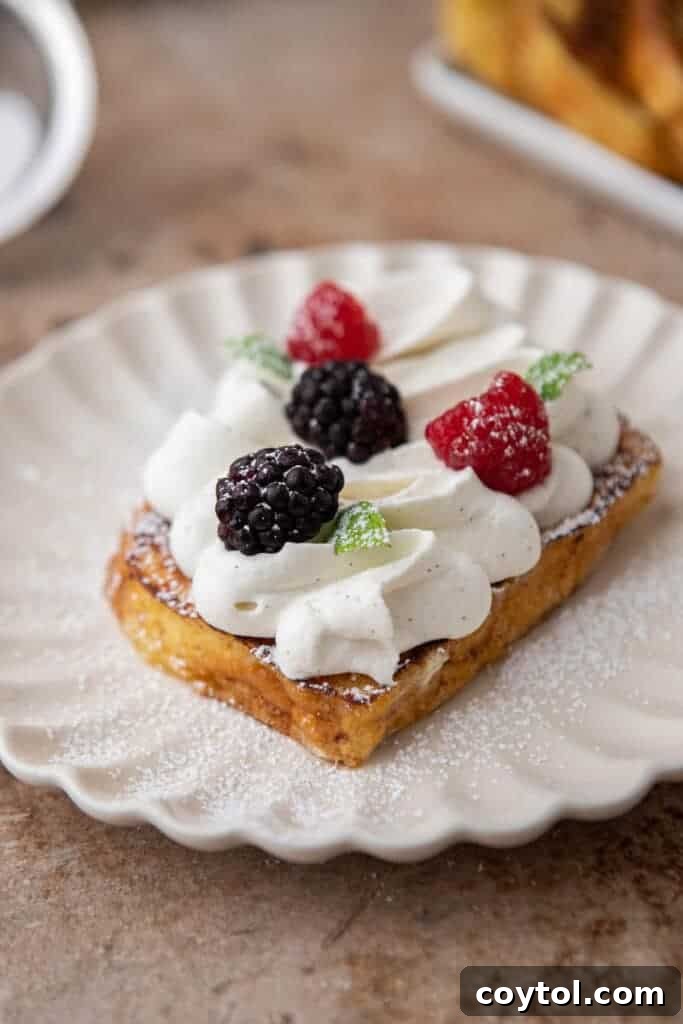 Brioche french toast stack topped with whipped cream, berries, and powdered sugar.