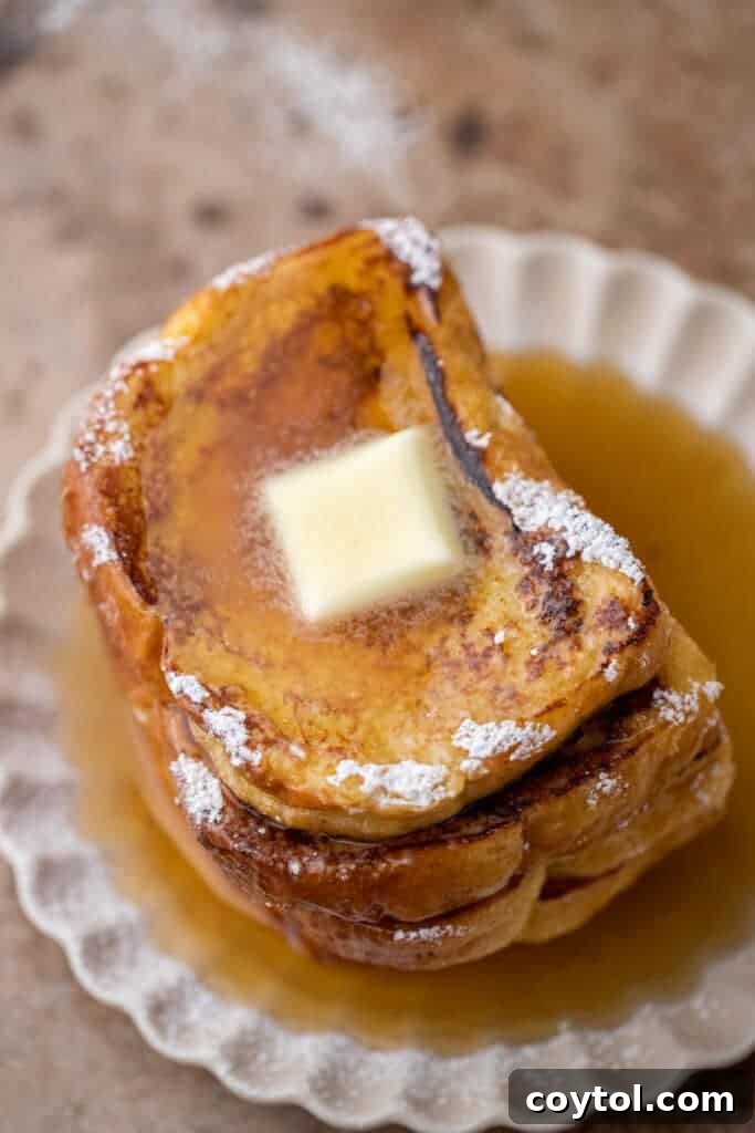 Overhead shot of a beautifully stacked plate of brioche french toast, drizzled with syrup and fruit.