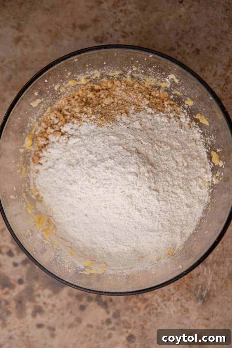 Divine Crumbl Lemon Cheesecake Cookies 5 Dry ingredients like flour, graham cracker crumbs, and leavening agents in a bowl, ready to be combined.