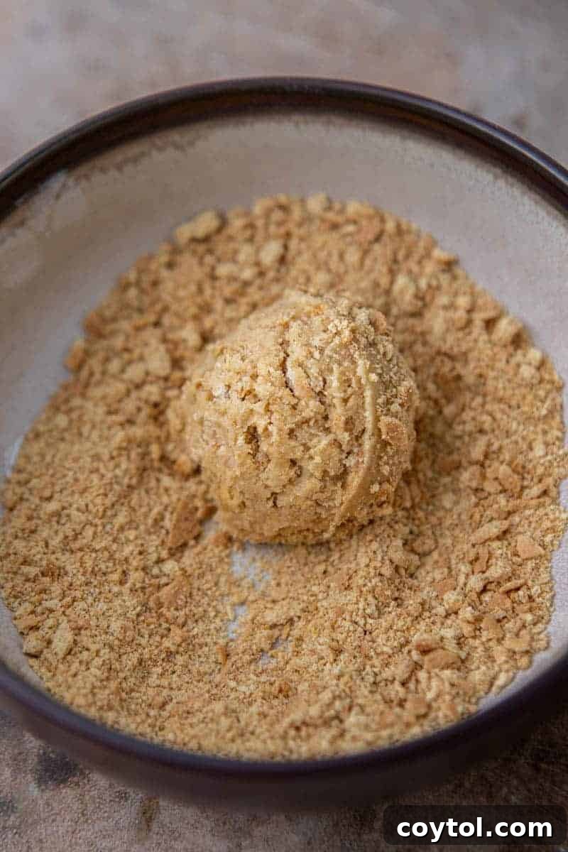 Divine Crumbl Lemon Cheesecake Cookies 7 A perfectly portioned cookie dough ball rolled in graham cracker crumbs, ready for baking.