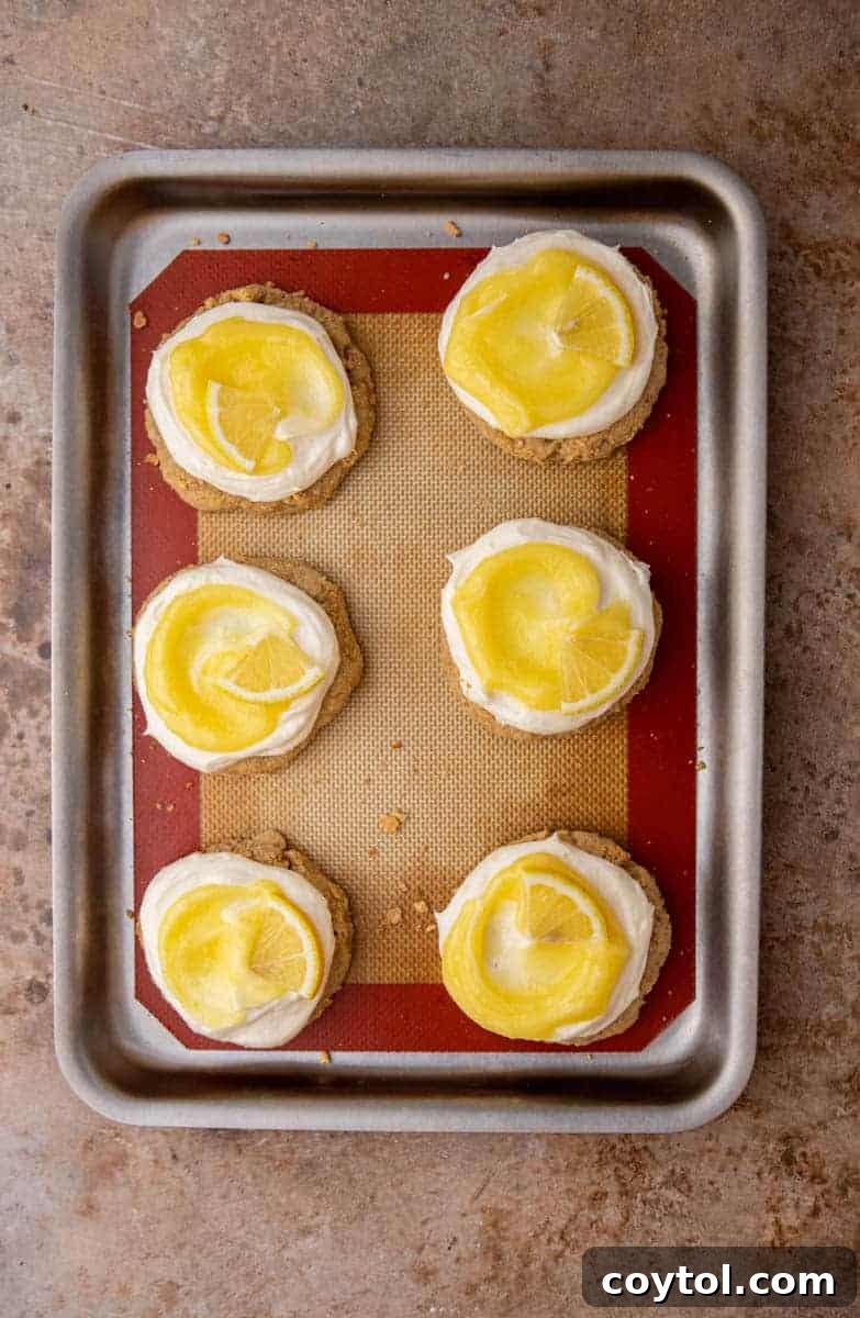 Divine Crumbl Lemon Cheesecake Cookies 9 A tray of beautifully frosted lemon cheesecake cookies, topped with lemon curd swirls and fresh lemon slices.