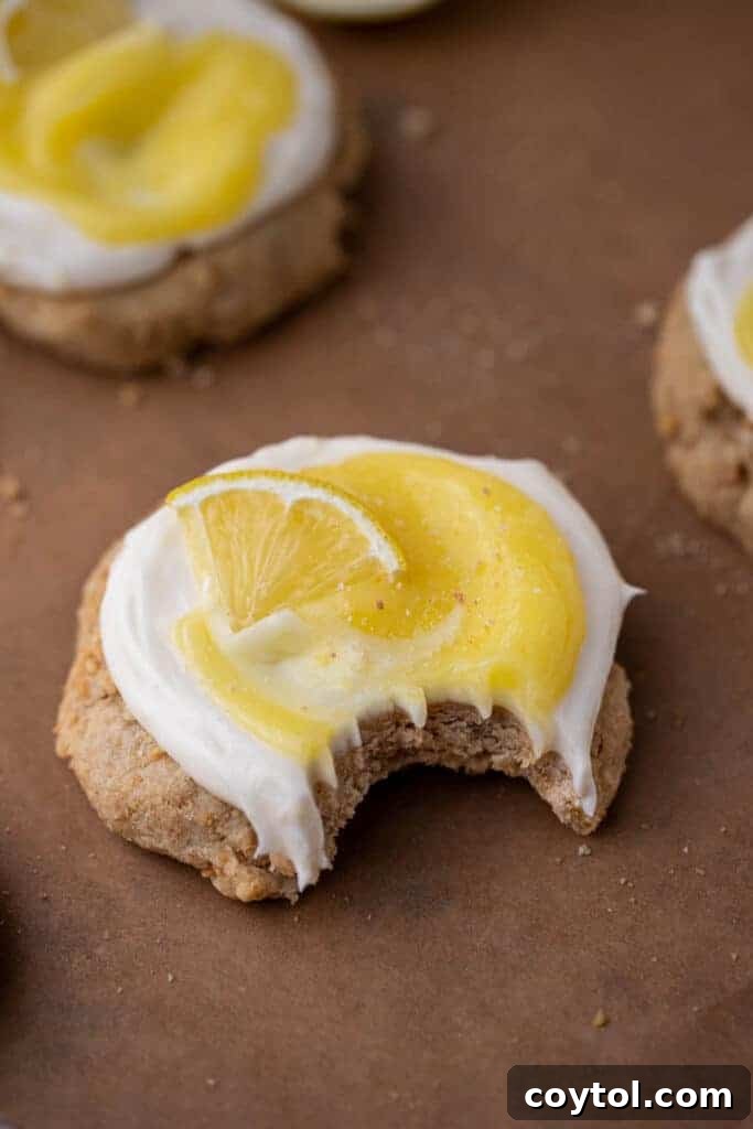 Divine Crumbl Lemon Cheesecake Cookies 10 A close-up of a Crumbl-style lemon cheesecake cookie with a bite taken out, showcasing the soft cookie base, creamy frosting, and tangy lemon curd.