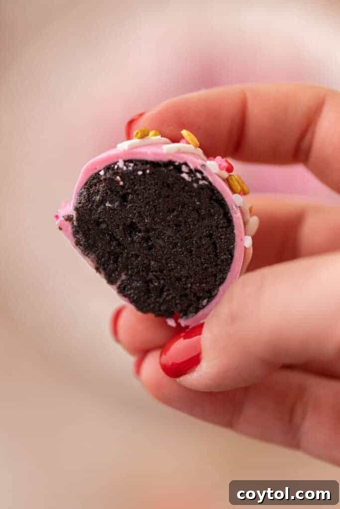 No-Fuss Valentine's Oreo Truffles 4 A hand gently holding a single, perfectly coated pink Valentine's Day Oreo truffle.