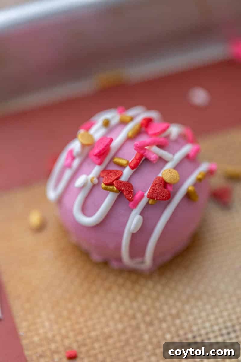 No-Fuss Valentine's Oreo Truffles 8 A pink Valentine's Day Oreo truffle with sprinkles, resting on a baking sheet.