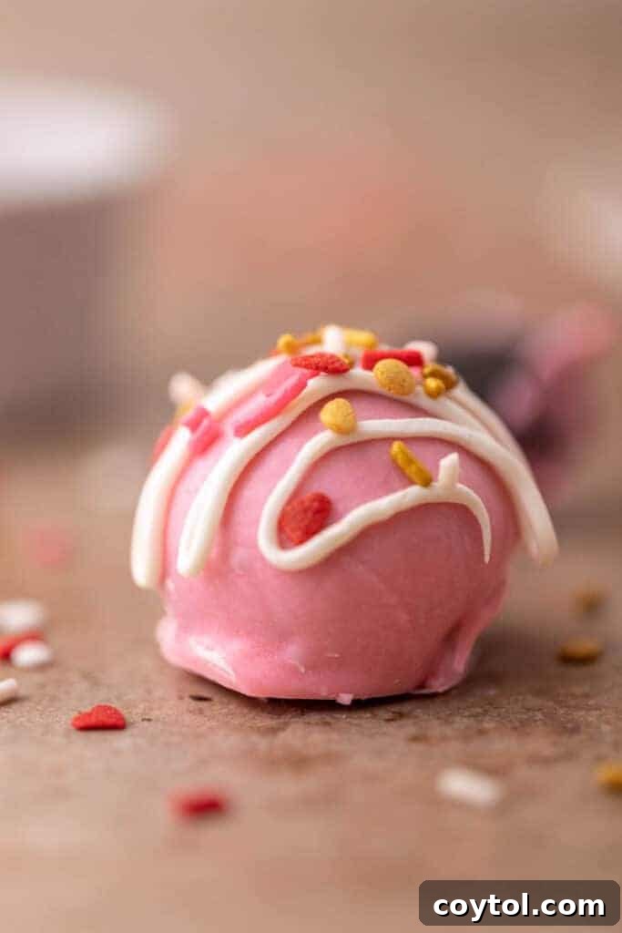 No-Fuss Valentine's Oreo Truffles 10 A straight-on shot of a perfectly coated pink Oreo truffle with delicate white chocolate drizzle and sprinkles.