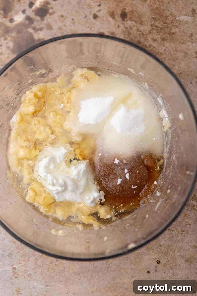 A bowl of wet ingredients for banana bread, including mashed bananas, oil, and sugars, perfectly mixed.
