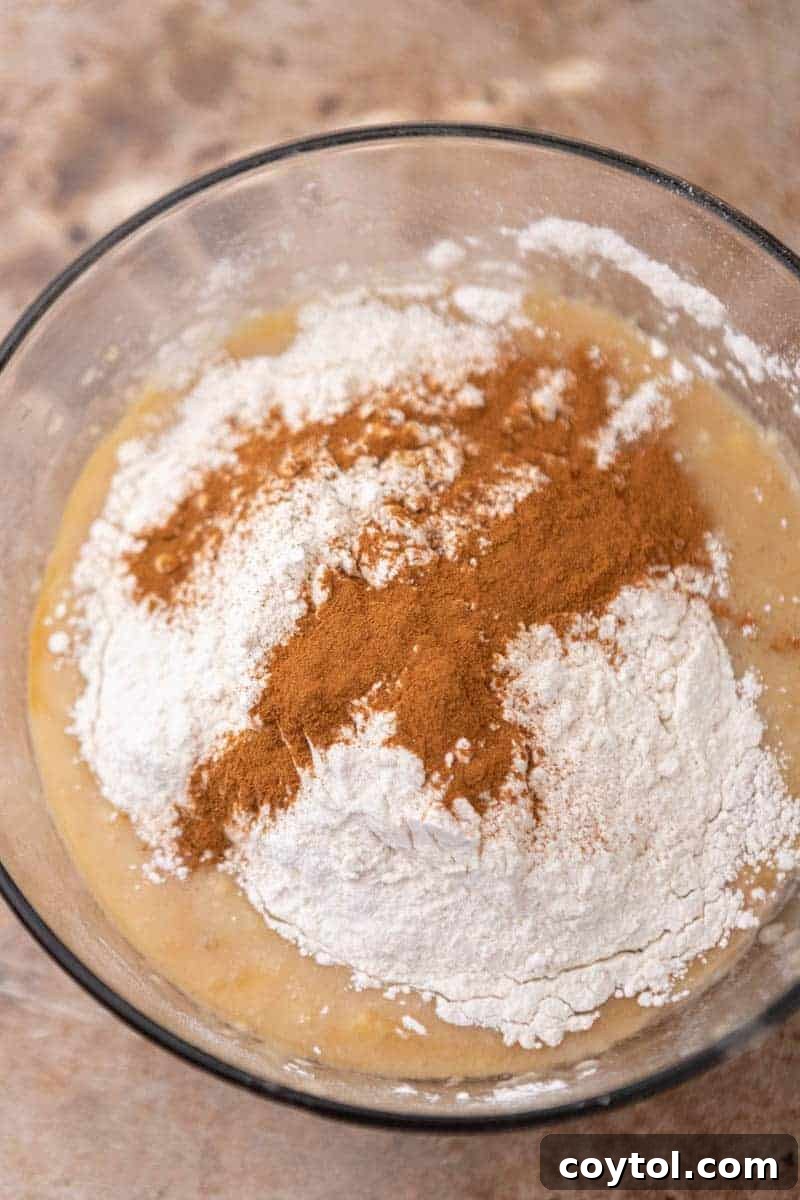 Dry ingredients like flour and spices being gently folded into the wet banana mixture.