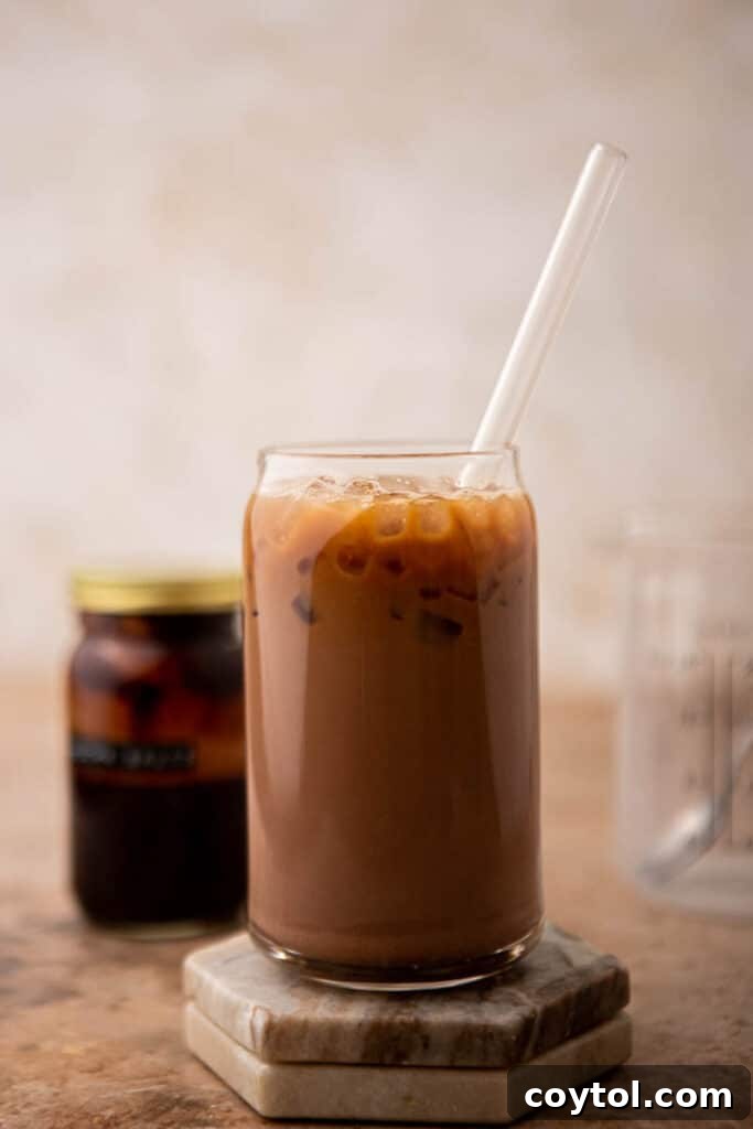 A tall glass filled with an iced mocha latte, garnished with chocolate syrup, sits on a rustic wooden surface, with coffee beans scattered around, highlighting the rich and inviting nature of the beverage.