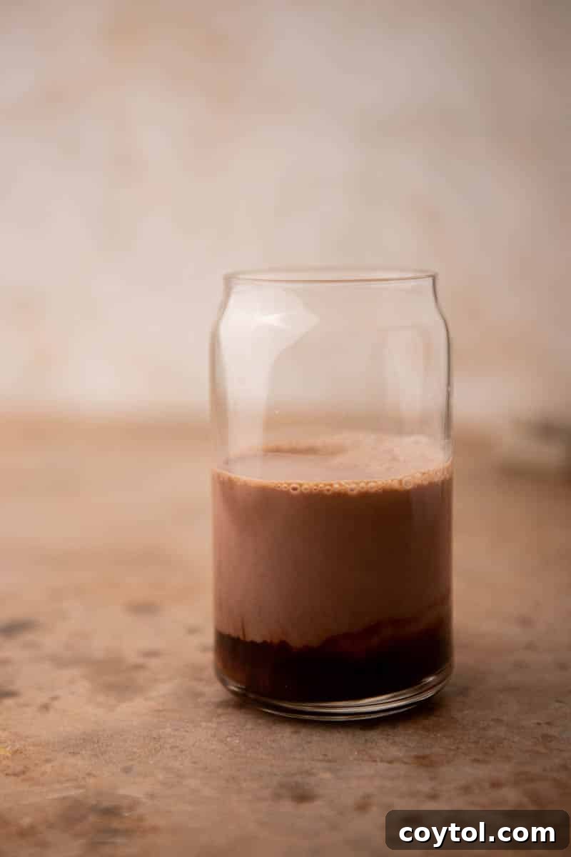Close-up of espresso and chocolate syrup being stirred together in a clear glass before adding milk and ice, showcasing the initial mixing step for an iced mocha latte.
