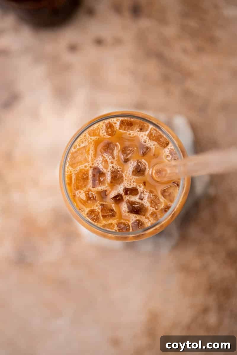 A hand pouring milk into a glass already containing mixed espresso and chocolate over ice, demonstrating the next step in preparing an iced mocha latte.