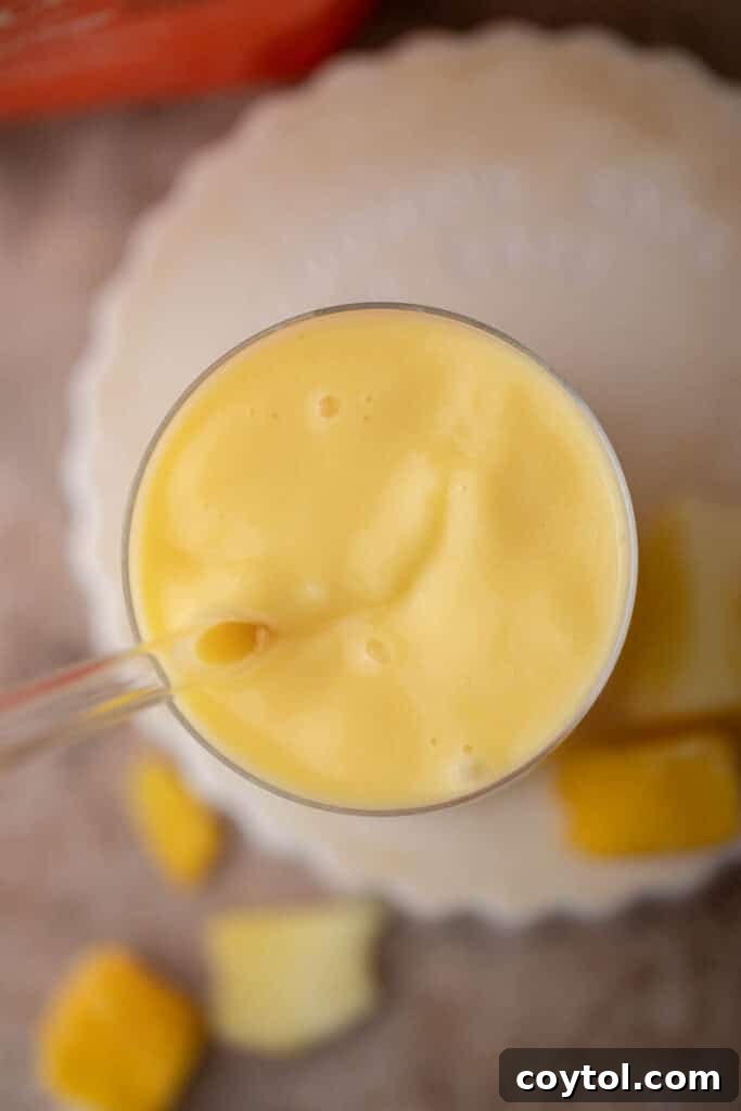 Overhead shot of a vibrant McDonald's mango pineapple smoothie in a glass with a straw.