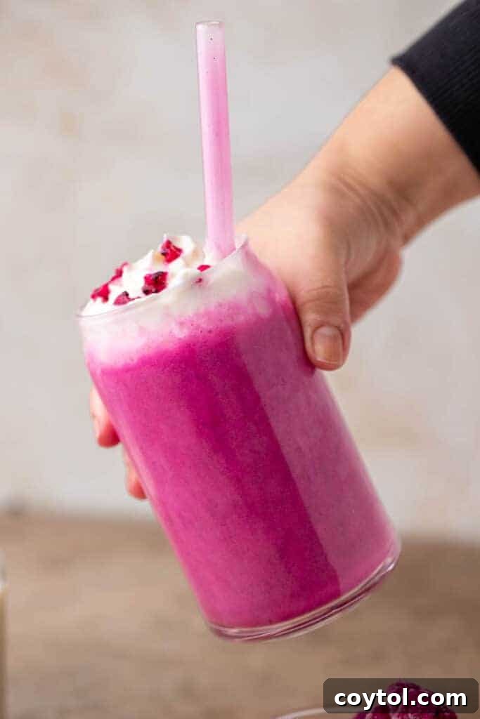 Hand holding a vibrant pink Starbucks Barbie frappuccino with whipped cream and dragon fruit topping