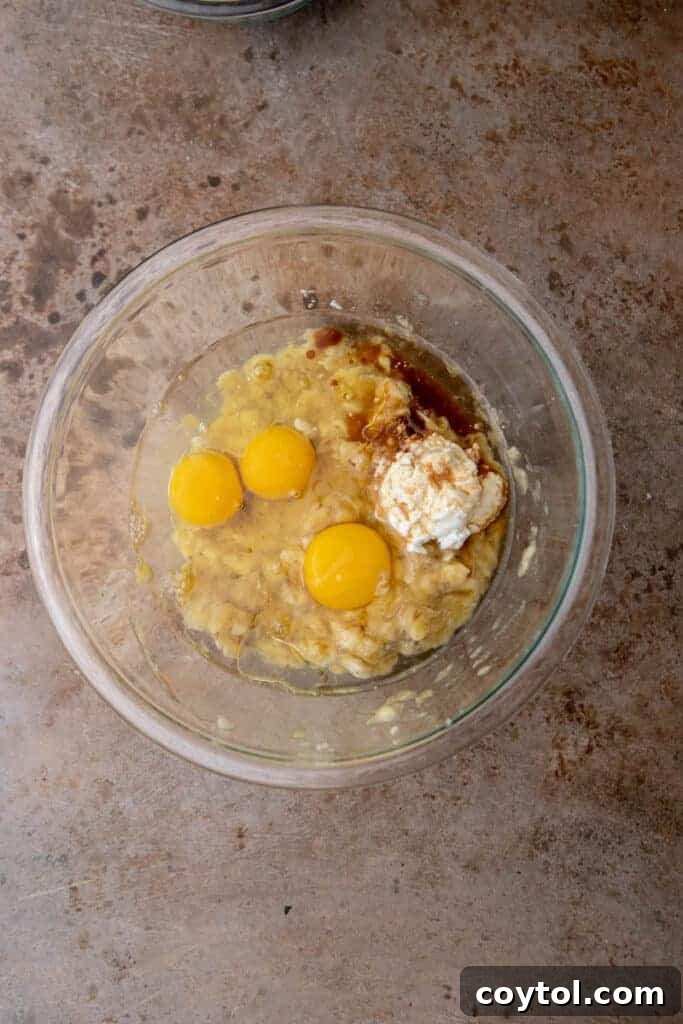 Mashed bananas and other wet ingredients being mixed in a large bowl.