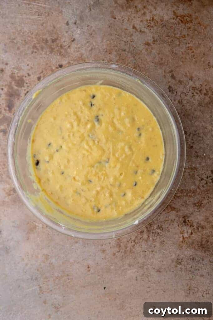 Cake mix and other dry ingredients being folded into the banana batter in a mixing bowl.