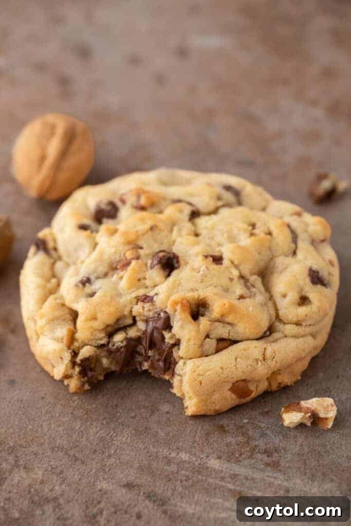 Close up of a single serve Levain chocolate chip walnut cookie with a bite taken out, revealing its gooey center