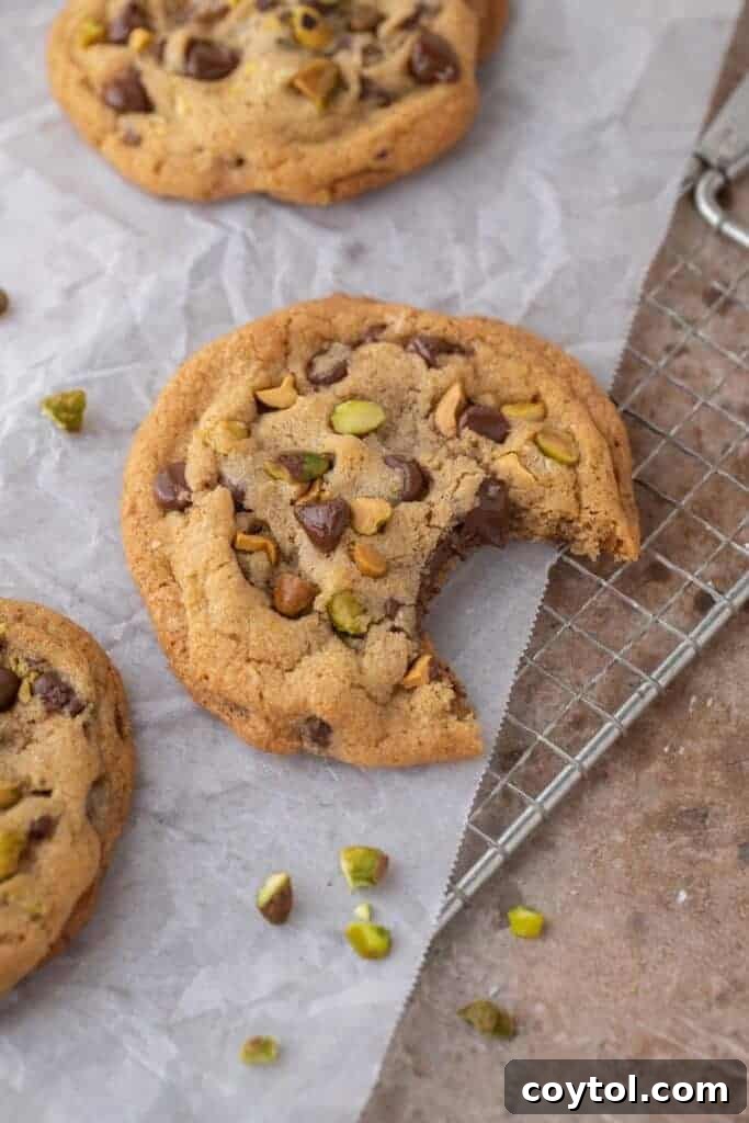 Decadent Brown Butter Pistachio Chocolate Chip Cookies 10 A brown butter pistachio chocolate chip cookie with a bite taken out, revealing its soft, chewy interior with melted chocolate and pistachios.