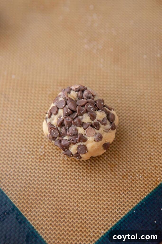 Cookie dough ball coated in an abundance of mini chocolate chips, ready for baking