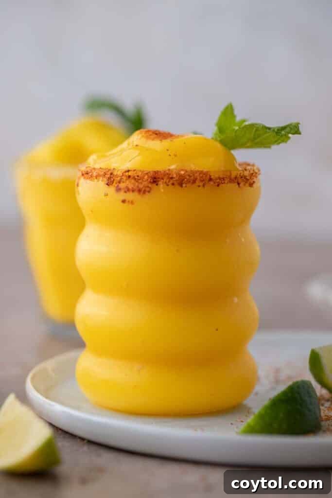 Frozen mango margaritas in elegant wiggly glasses, garnished with lime and a salted rim.