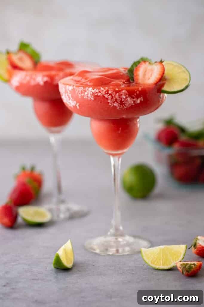A frosty glass of frozen strawberry margarita garnished with a fresh strawberry and lime slice.
