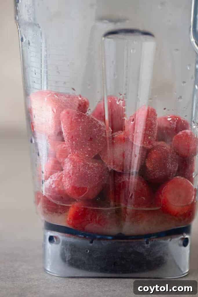 Close-up of fresh strawberries, lime, and tequila in a blender before blending.