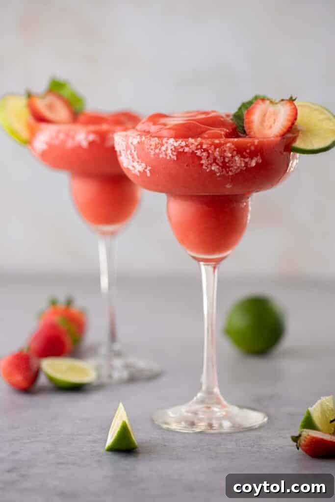 A close-up of a beautifully garnished frozen strawberry margarita in a glass.