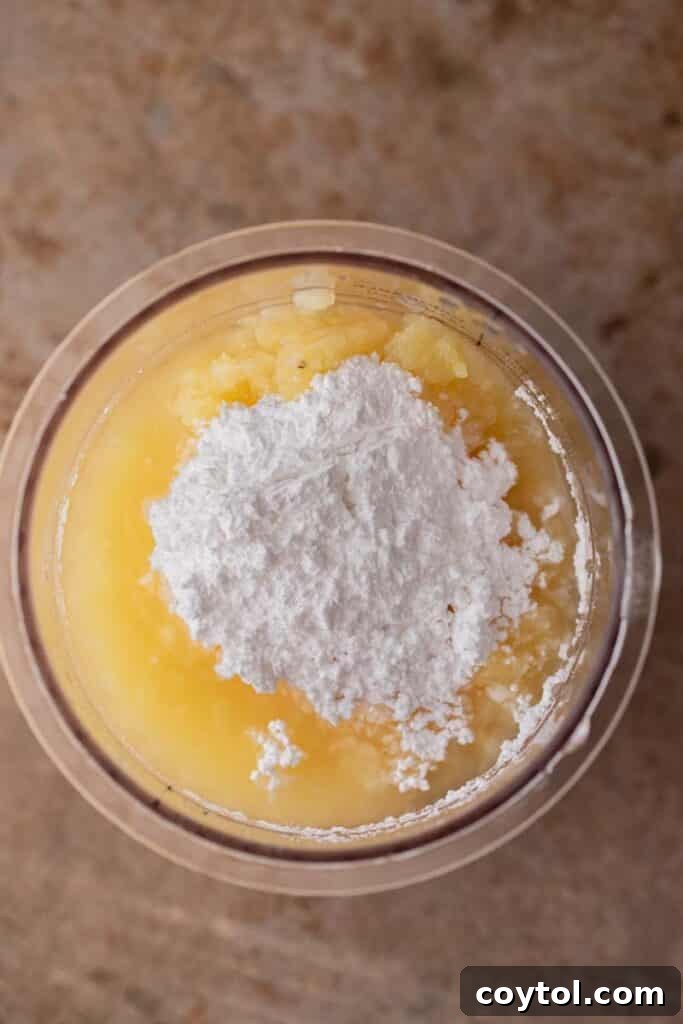 Crushed pineapple being poured into a Ninja Creami pint cup