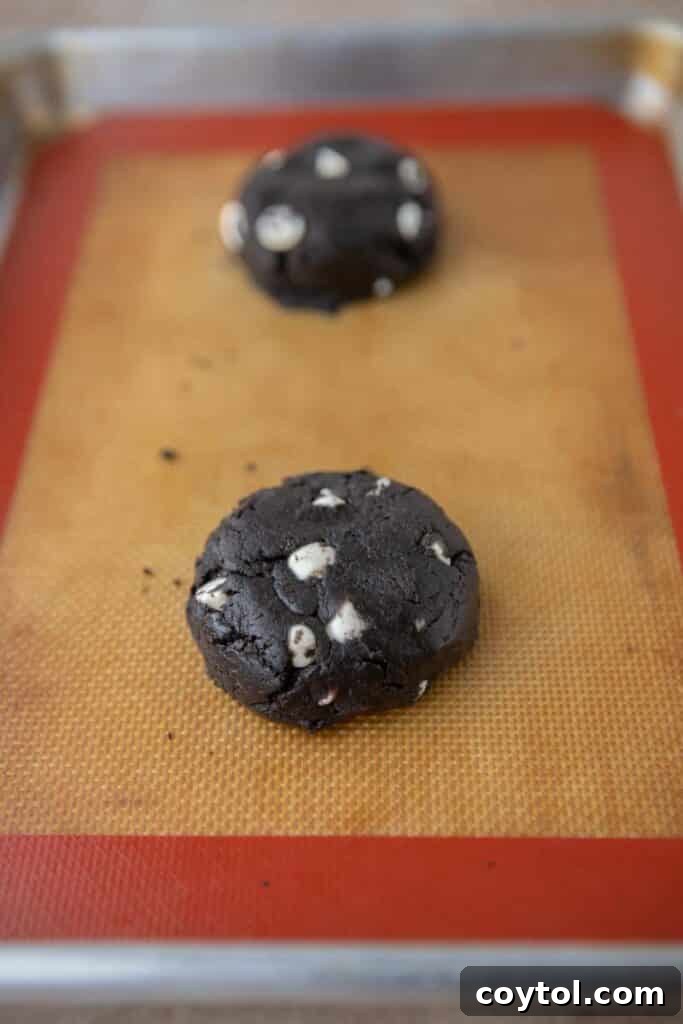 Crumbl Chocolate Cookie Cream Bliss 8 Scooped cookie dough balls flattened on a parchment-lined baking sheet