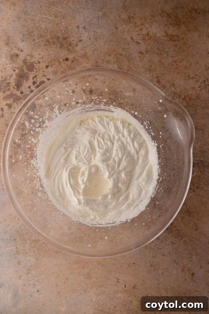 Freshly whipped heavy cream in a large mixing bowl, forming stiff peaks, a crucial step for no-churn ice cream.