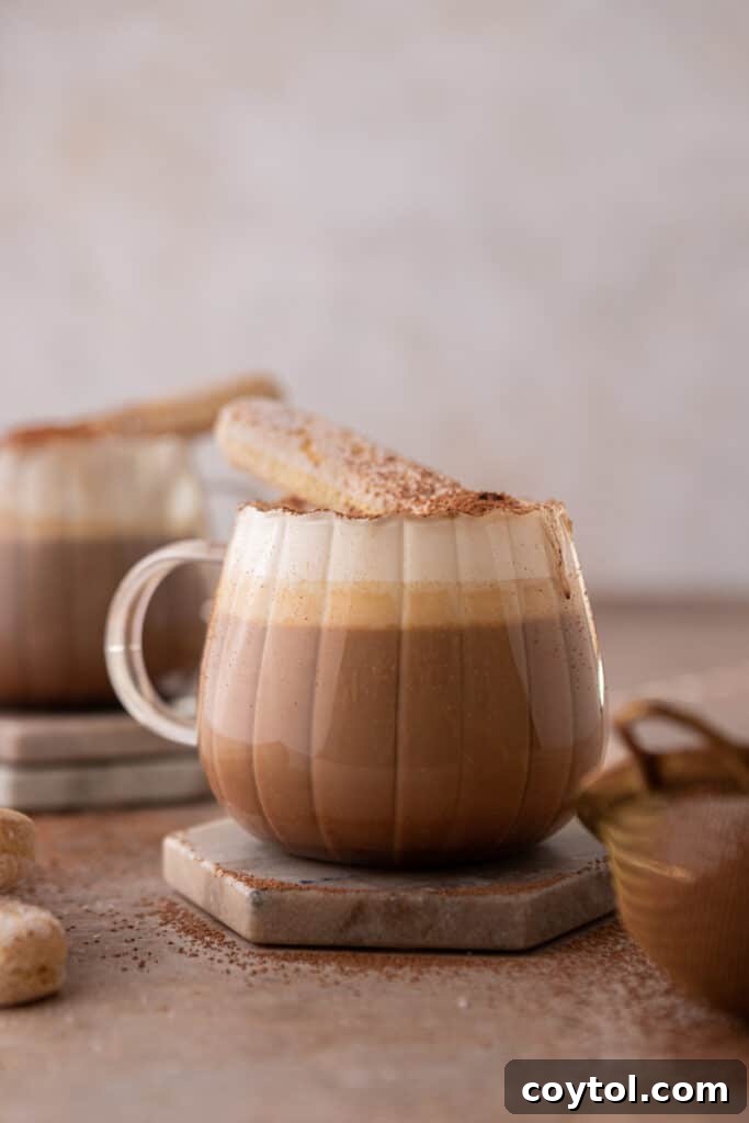 Cup with hot tiramisu latte in it, topped with cream and cocoa powder.
