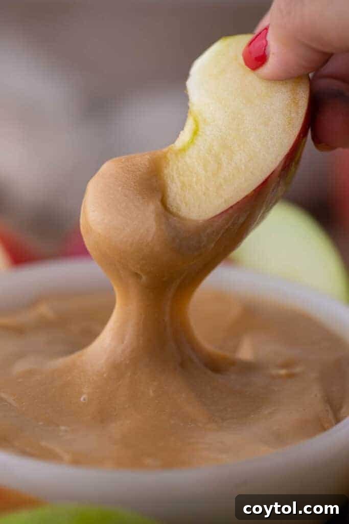 Crisp apple slice dipped generously into rich, golden homemade caramel sauce, highlighting its thick and smooth texture.