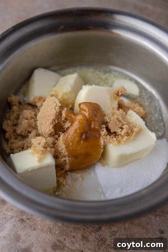 Granulated sugar, brown sugar, corn syrup, and butter being combined in a saucepan on the stovetop.