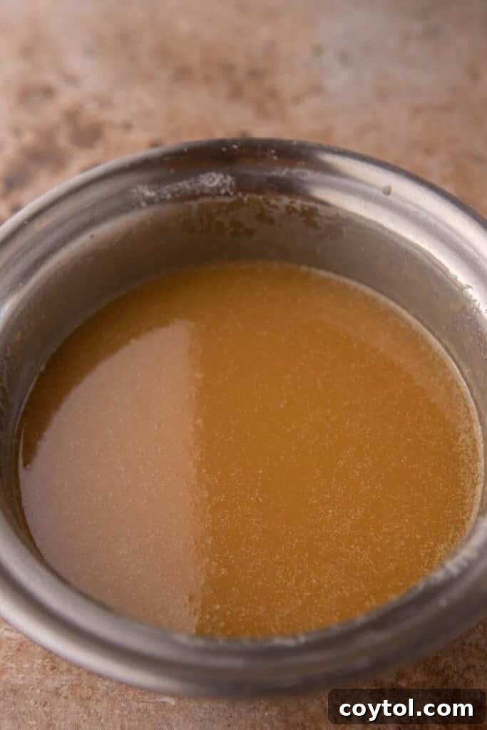 Thick, glossy homemade caramel sauce being stirred in a saucepan after all ingredients are combined, ready to cool.